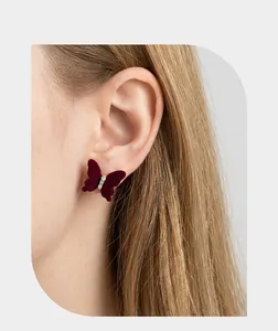Close-up of a burgundy velvet butterfly stud earring with tiny crystals on an ear