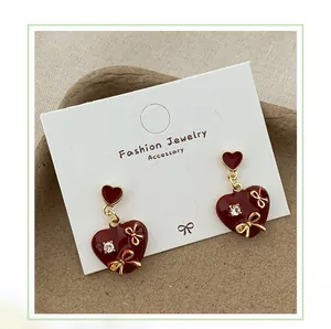 Detail of red enamel heart earrings with gold bows and diamond stud on display card