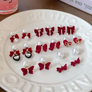 Set of burgundy velvet bow earrings with pearls and gold heart charms on a white plate