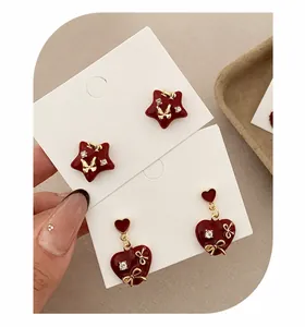 Macro detail of dark red enamel heart and star earrings with golden bow accents