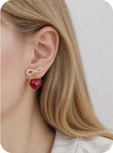 Close-up of red heart earrings with pearl bow design worn by a model for elegant look