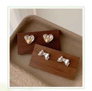 Detail of silver bow and heart earrings featuring textured finish and mixed metal tones