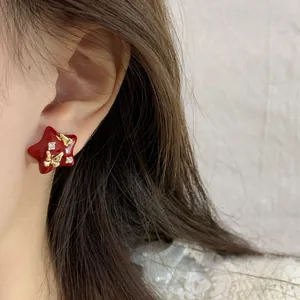 Star-shaped red enamel earrings with gold foil and crystals worn by a model