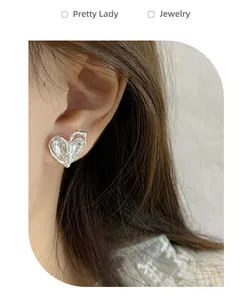 Close-up of heart-shaped silver earrings with transparent zircon on model ear