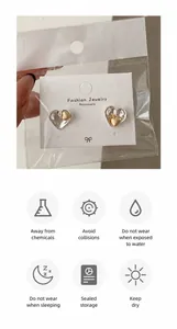 Detail view of heart earrings in gold and silver finish with jewelry care instructions
