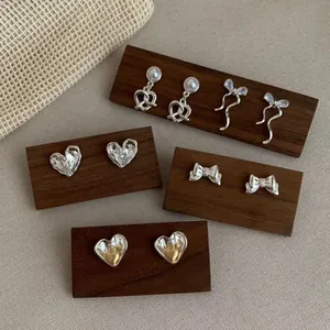 Minimalist silver heart and bow earrings set on a wooden display stand for women