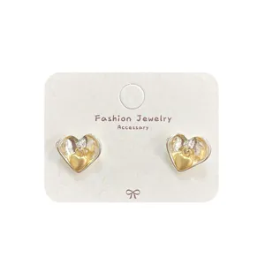 Elegant silver heart earrings with textured gold bow details on a white jewelry card