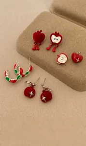 Detail view of red flocked and enamel apple earrings in various festive creative designs