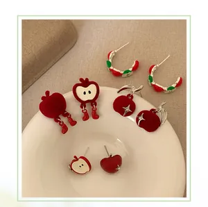 Detail of red flocked apple earrings and festive stud designs on a white ceramic plate