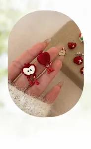 Detail of red flocked apple earrings with asymmetric design and mini boot pendants