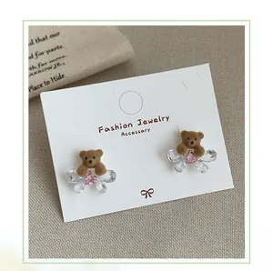 Macro view of brown flocked bear stud earrings with crystal bows on a jewelry card