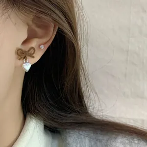 Orecchini a fiocco marrone floccato con pendenti a cuore argento su una modella
