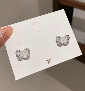 Makroaufnahme funkelnder Schleifen-Ohrstecker mit Kristallen und Perlen auf Schmuckkarte