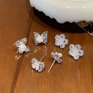 Funkelnde Kristall-Blumen- und Schmetterlings-Ohrstecker auf dunklem Holzgrund