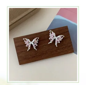 Dettaglio di orecchini a farfalla con zirconi rosa e montatura in argento su legno
