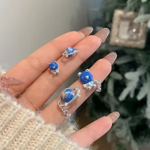 Set di orecchini a forma di orsetto blu stellato e pianeta mostrato sulle dita