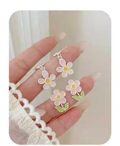 Detail of pink sunflower earrings set with enamel petals and silver base held in hand