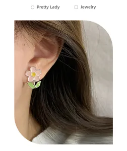 Close-up of pink sunflower earrings with green leaves worn on a female ear