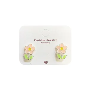 Pink sunflower earrings with green leaves on white jewelry card for spring fashion