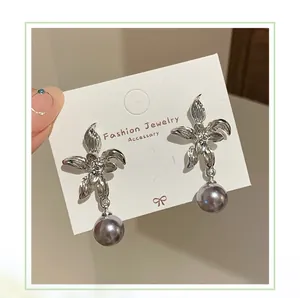 Macro shot of silver flower earrings with textured petals and dangling gray pearls