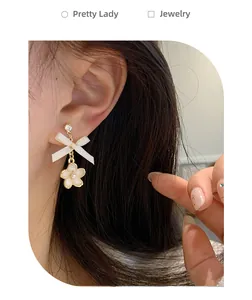Close-up of sweet bow and flower drop earrings with crystals worn by a model
