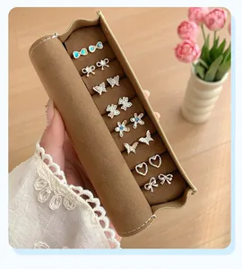 Brown velvet jewelry roll organizer showcasing eight pairs of silver-toned stud earrings