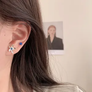 Silver flower stud earrings set with blue gemstones worn on ear for women