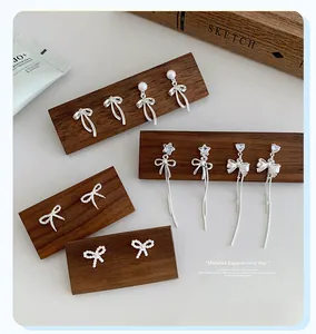 Detailed collection of silver bow earrings with long tassels and pearls on wood