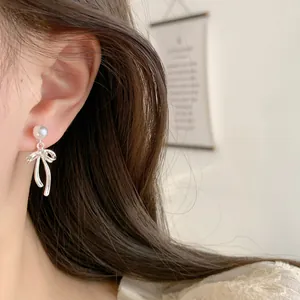 Elegant silver bow earrings with pearl studs and long tassels on female model