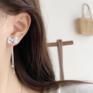 Light blue fabric bow earrings with silver tassel chains on female model's ear