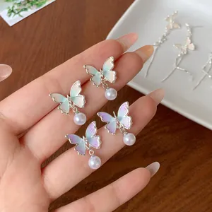 Elegant gradient enamel butterfly earrings with hanging pearl drops in a natural setting