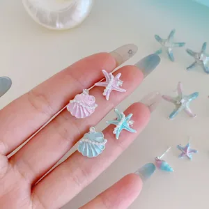Orecchini a stella marina e conchiglia blu e rosa con perle e strass tenuti in mano