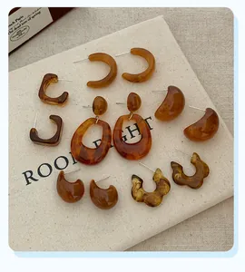 Detailed flat lay of amber resin geometric earrings and C-hoops on beige fabric board
