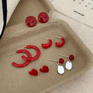 Five pairs of cherry red geometric hoop earrings and heart studs in a rustic tray