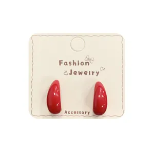 Glossy cherry red geometric hoop earrings with a teardrop shape on a display card