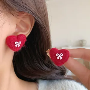 Red plush heart-shaped stud earrings with white bow detail for festive winter wear