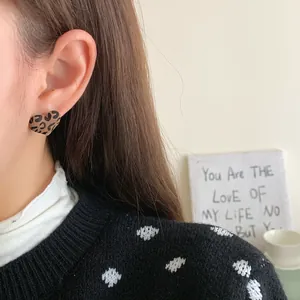 Elegant heart-shaped leopard print earrings worn by a model in a cozy winter setting