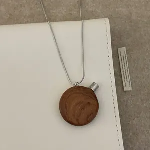 Vue détaillée du pendentif flacon de parfum en bois vintage sur une chaîne serpent fine