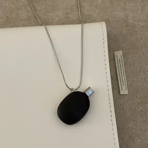Collier rétro avec pendentif galet noir et chaîne argentée sur un carnet blanc
