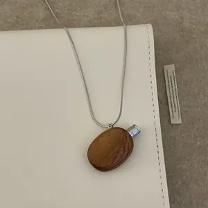 Détail du pendentif flacon de parfum en bois vintage sur une chaîne serpent argentée élégante