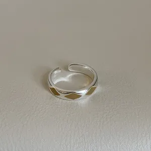 Detail of silver open ring featuring golden diamond pattern accents and smooth metal finish