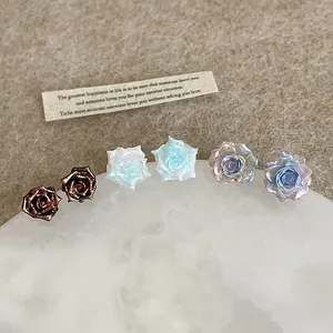 Detailed view of three resin rose stud earrings in bronze, ice blue and purple blue
