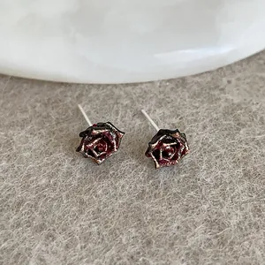 Macro detail of dark red rose earrings with gold edges on a gray velvet surface