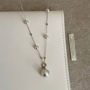 Detalle de collar de perlas plateado con un gran colgante de perla sobre cuero blanco