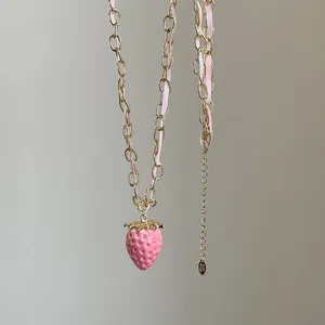Detalle del collar con colgante de fresa rosa con cadena dorada y cinta tejida