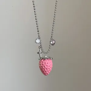 Detalle de un collar de cuentas plateadas con colgante de fresa rosa y dijes de estrella