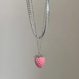 Detalle de collar de doble capa con colgante de fresa rosa y cadena de tenis de circonia