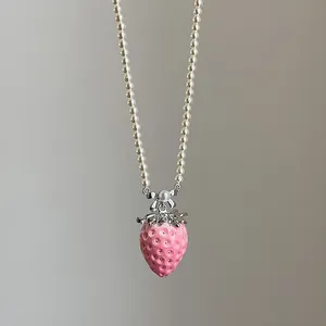 Detalle del colgante de fresa rosa con lazo de plata en collar de perlas blancas