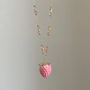 Detalle macro del collar con colgante de fresa, cuentas rosas y textura de hoja dorada