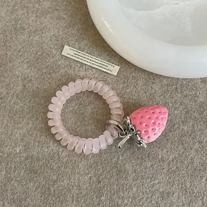 Detalle de un dije de fresa rosa en un coletero en espiral mate sobre una textura de fieltro
